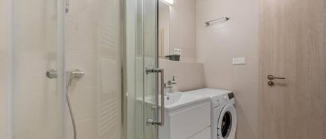 A bathroom with a glass shower enclosure, a sink, and a washing machine.
