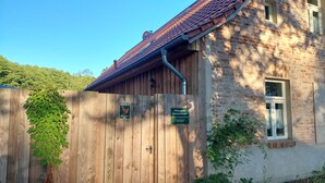 Een houten hek, een bakstenen gebouw met een pannendak en een raam.