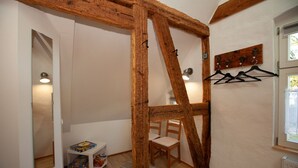 Een kamer met zichtbare houten balken, een witte muur, een tafeltje met een doos, een stoel en een radiator.