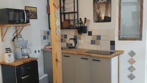 Een praktische keuken met een magnetron, koffiezetapparaat en broodrooster. Er is een kleine koelkast, houten kastjes en een houten kruk.