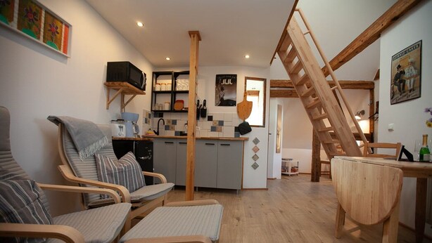 Een gezellige woonkamer met een houten trap, een keuken met een betegelde achterwand en een eethoek met een houten tafel.