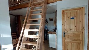 Een houten trap die leidt naar een verdieping, een houten deur met een bordje en een keuken met kasten en een gootsteen.