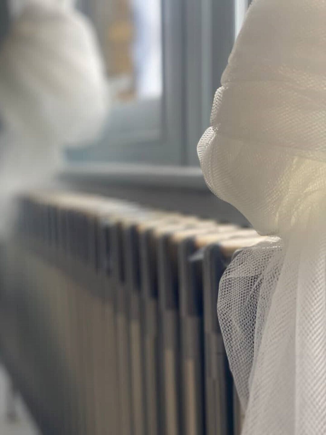 A close-up of a white knitted fabric, likely part of a garment, with a blurred background featuring a radiator.