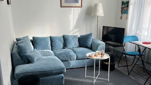 Una sala de estar moderna con un sofá seccional azul, una mesita redonda, un televisor y una silla plegable.