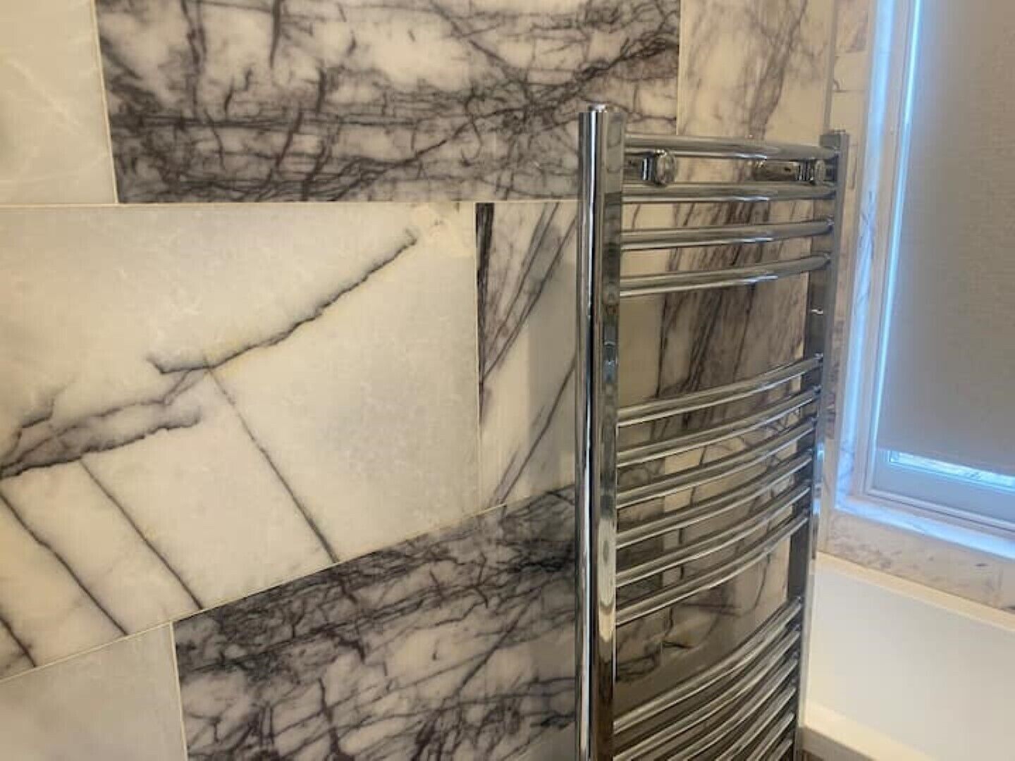 Een badkamer met een chromen handdoekrek en marmeren tegels.
