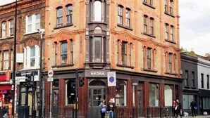 Un edificio en esquina con un letrero que dice "NKORA" y un letrero que indica "Prohibido Estacionar".