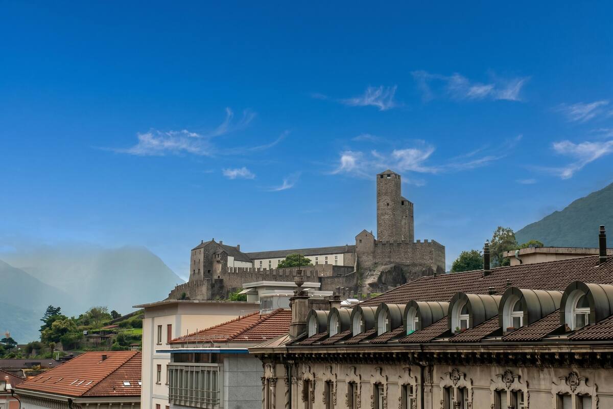 A historic building with a prominent tower, surrounded by modern buildings with red-tiled roofs.