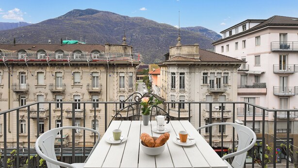 Un balcon avec une table dressée pour deux personnes, une plante en pot et une vue sur une montagne.