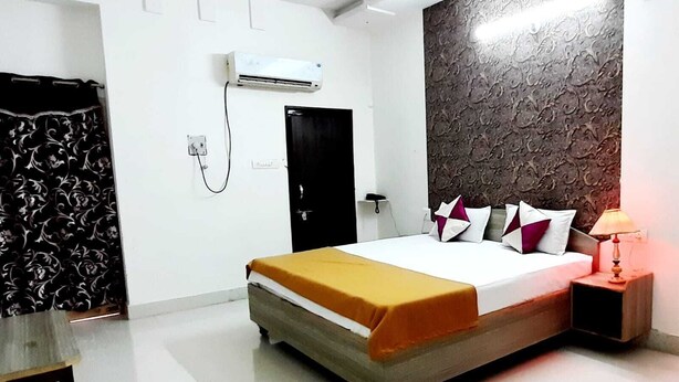 A hotel room with a bed, a bedside table, a lamp, a wardrobe, and an air conditioning unit. - Hotel Santosh (Jodhpur)