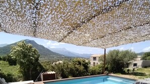 Ein Poolbereich mit Bergblick, eine Holzterrasse und ein überdachter Sitzbereich mit einer Laterne.