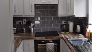 Cocina compacta con armarios blancos, horno empotrado, lavamanos y salpicadero de azulejos.