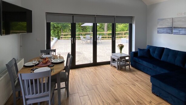 Amplia sala de estar con una mesa de comedor dispuesta para cuatro personas, un sofá azul y un ventanal que ofrece vistas al exterior.