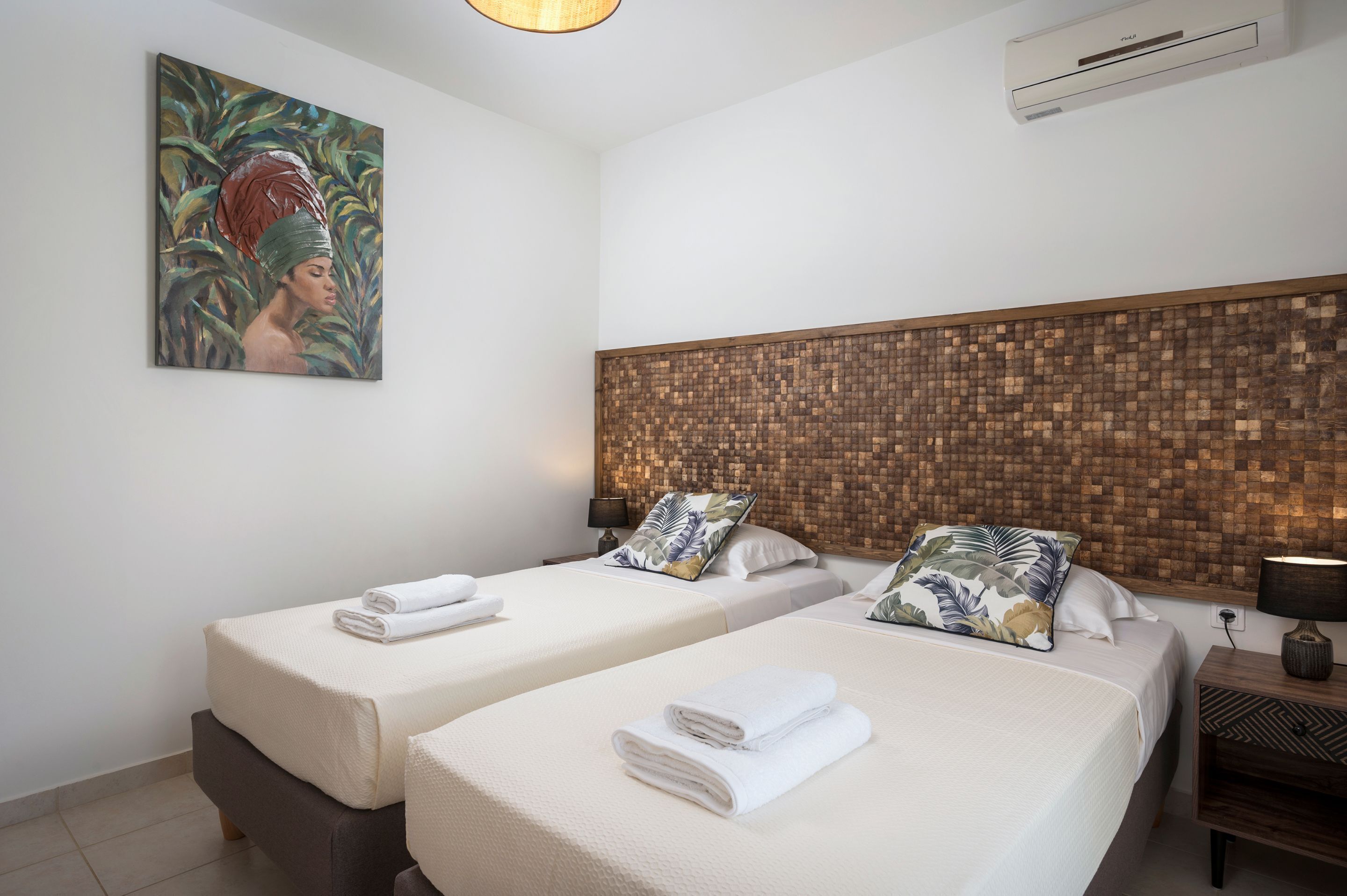 A hotel room with two beds, a painting on the wall, an air conditioning unit, and a wooden headboard.