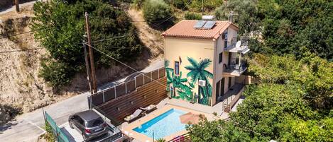 A residential property with a swimming pool, a car parked in the driveway, and a mural on the side of the house.
