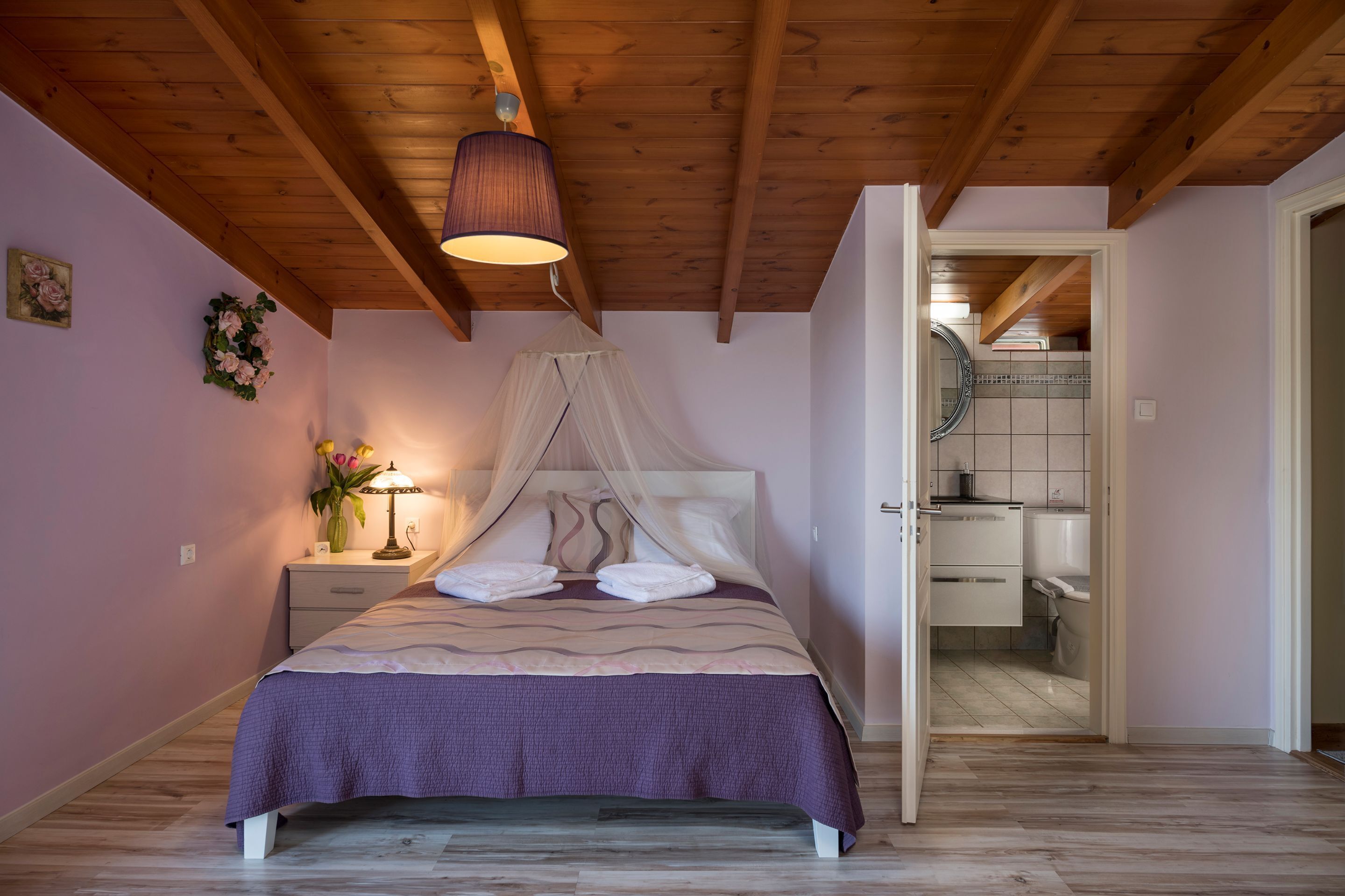 Ein Schlafzimmer mit Bett, Nachttisch, Lampe und Blick ins Badezimmer.