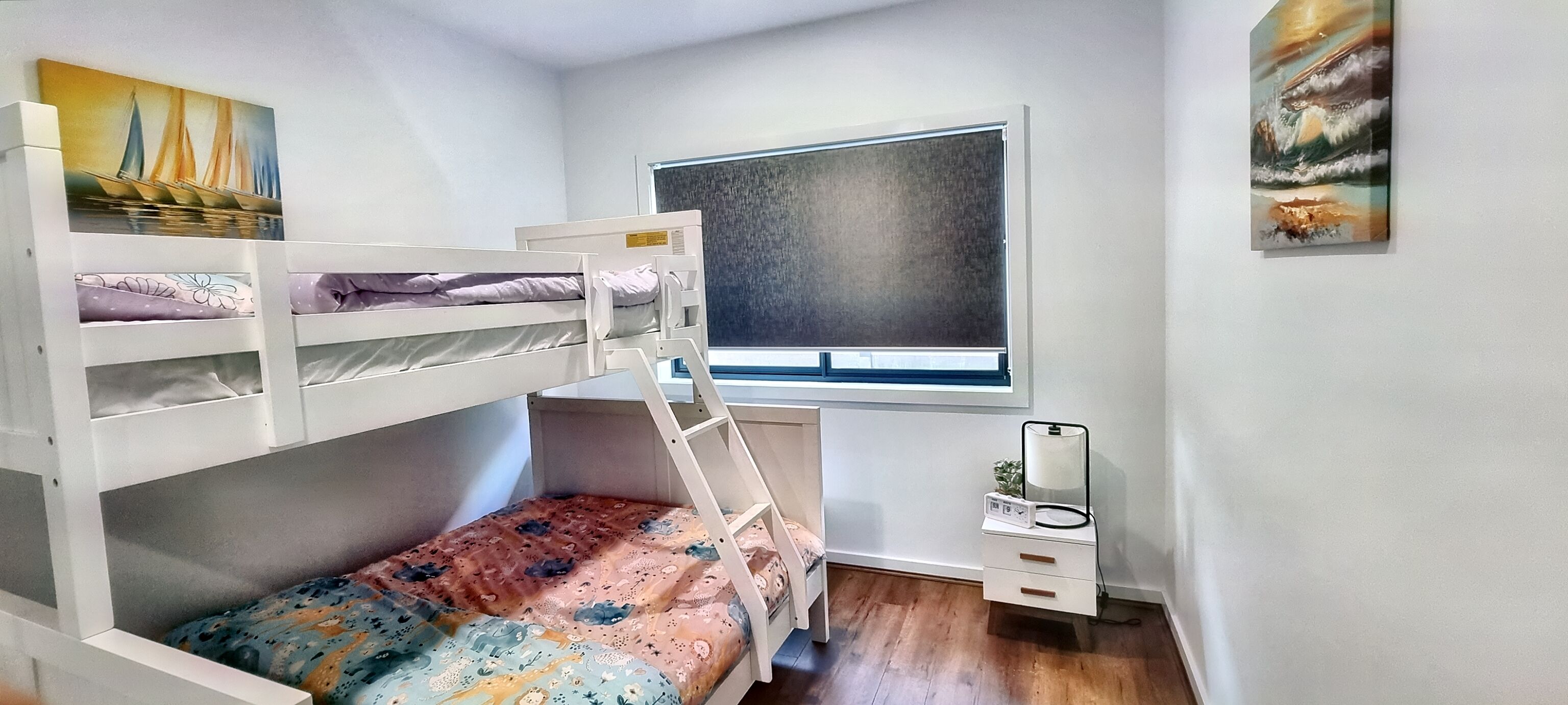 Un lit superposé avec une échelle, un bureau avec une chaise, une fenêtre et une table de chevet avec une lampe.