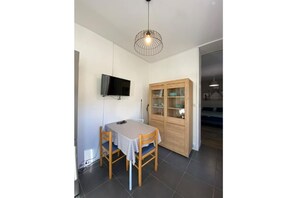 Un comedor con una mesa y sillas, un televisor montado en la pared y un mueble de madera con puertas de cristal.