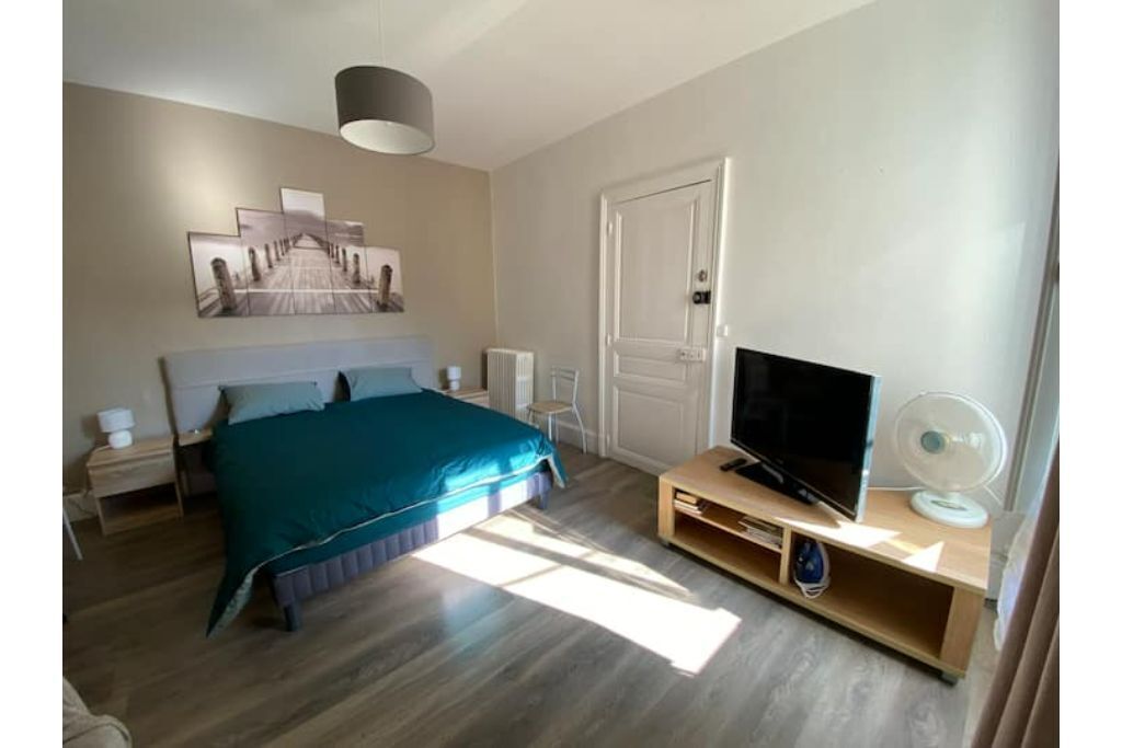 A bedroom with a bed, a TV, a fan, and a door.