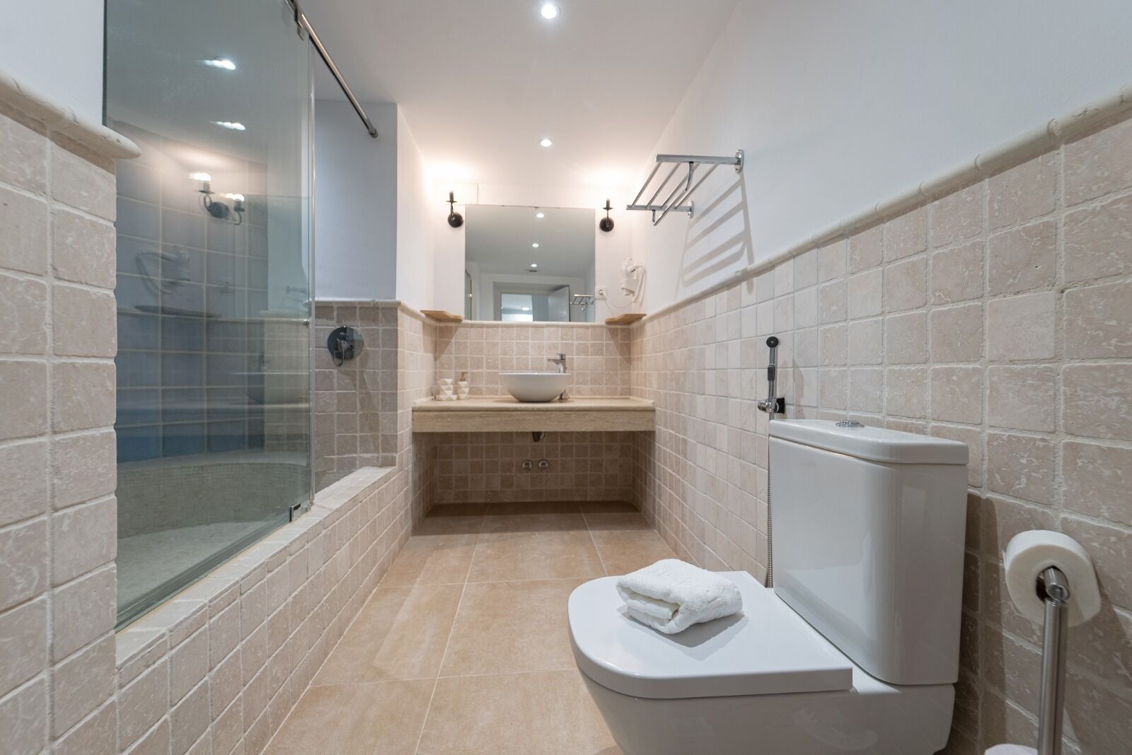 Un bagno moderno con box doccia in vetro, un lavandino bianco con lavabo a incasso e un water con un asciugamano sopra.