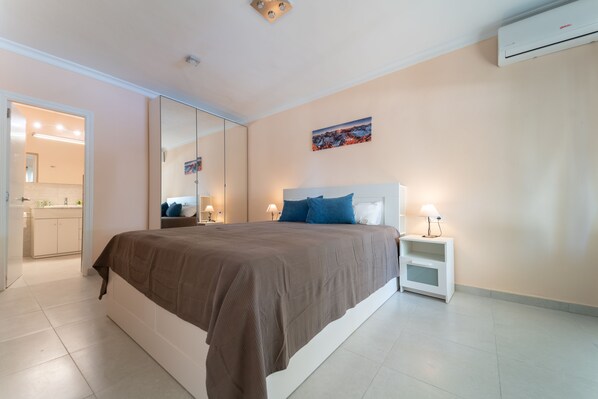 Un dormitorio con una cama grande, mesitas de noche, un espejo y un equipo de aire acondicionado.