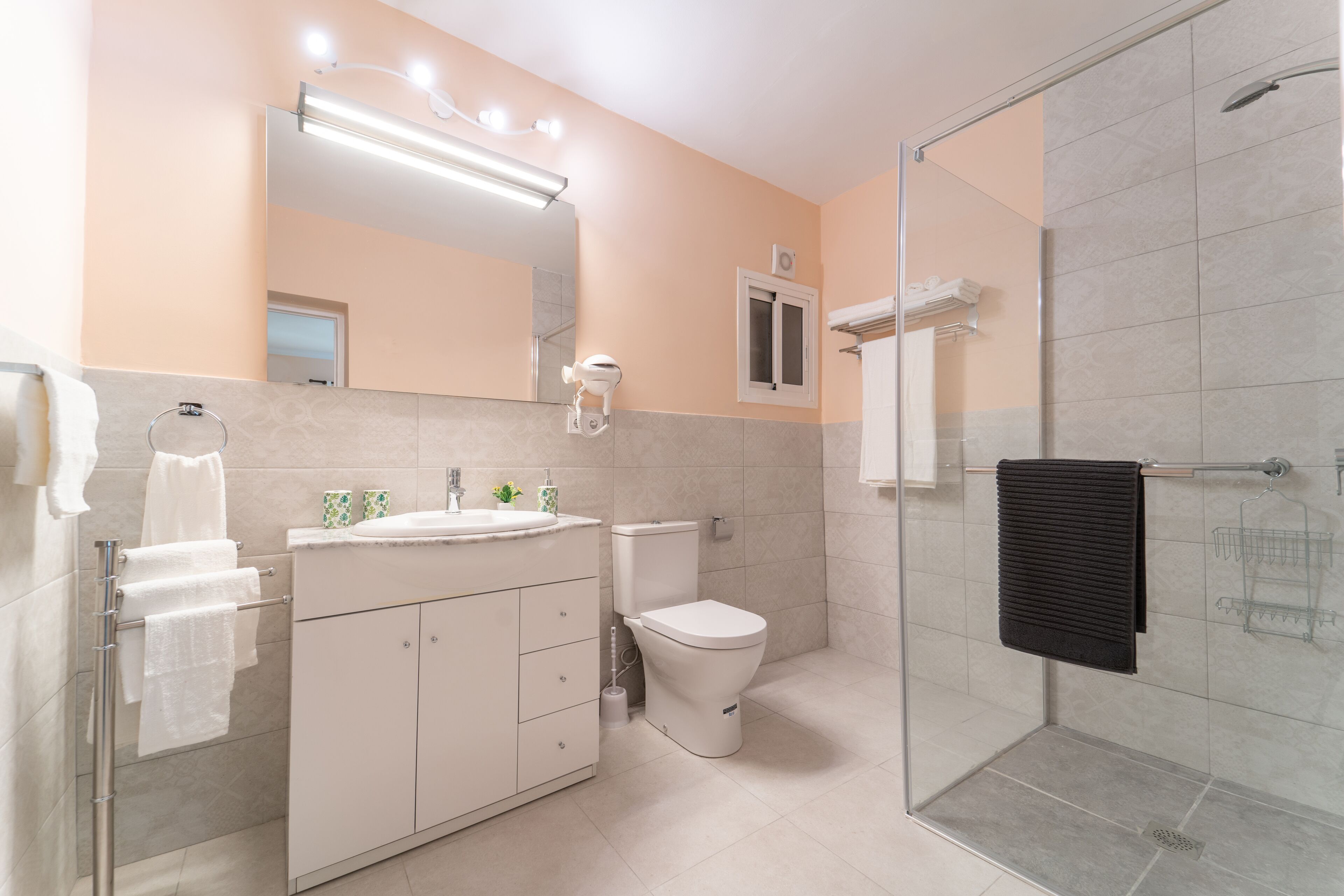 Une salle de bain moderne avec une douche à parois de verre, des toilettes blanches et un meuble-lavabo doté d’un miroir et d’un éclairage.