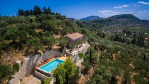 Eine Villa mit Swimmingpool, umgeben von Bäumen und einer Steinmauer.