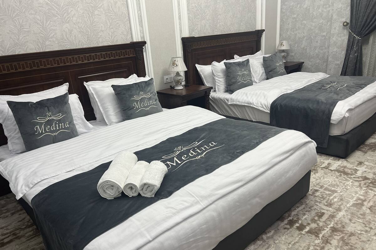 A hotel room with two beds, each with dark and light bedding, and pillows with the name 'Medina'.
