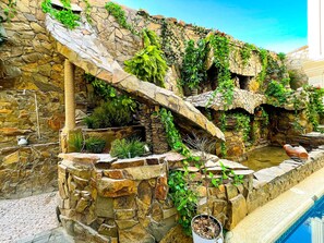 A stone wall with a small pool and plants. - Medina Hotel Samarkand (Samarkand)