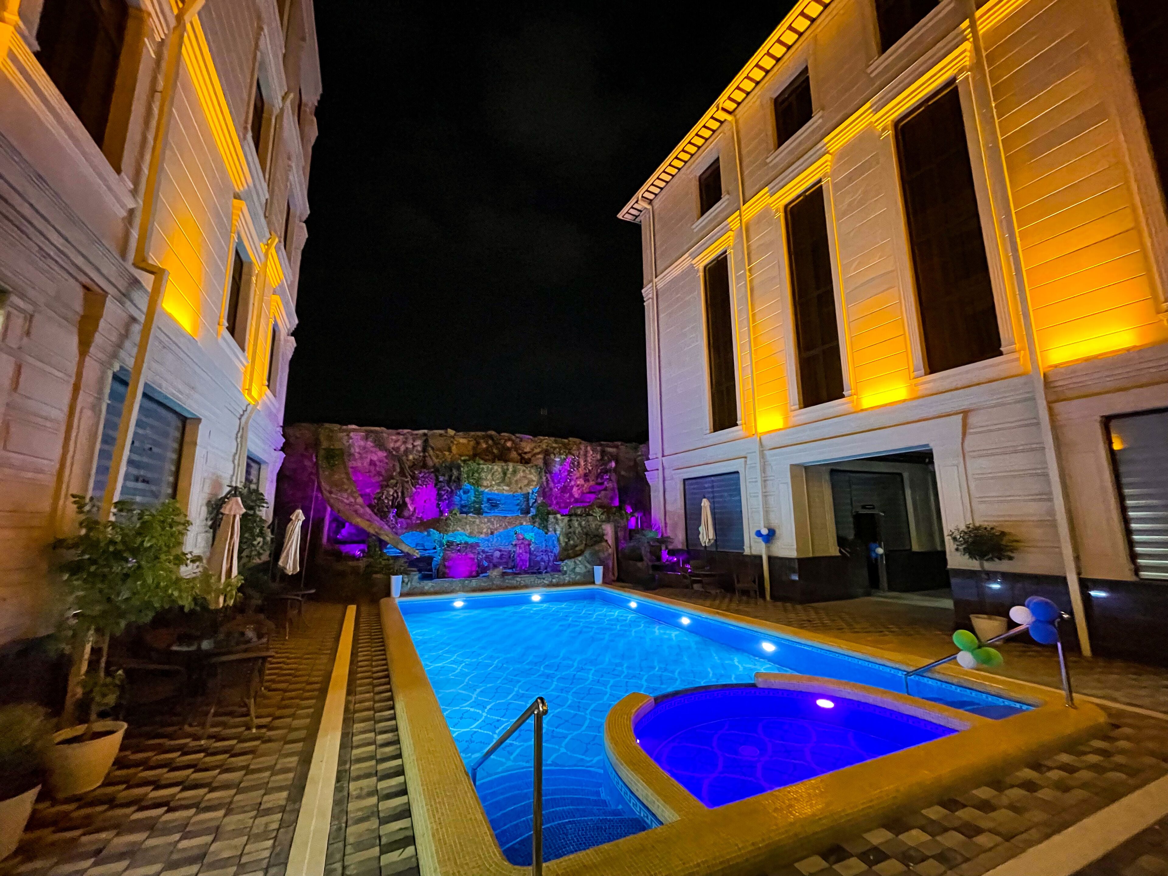A swimming pool with a blue water feature, surrounded by a paved walkway and potted plants.