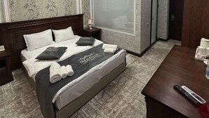Een moderne hotelkamer met een groot bed, een houten nachtkastje, een bureau met afstandsbediening en een plafondlamp.