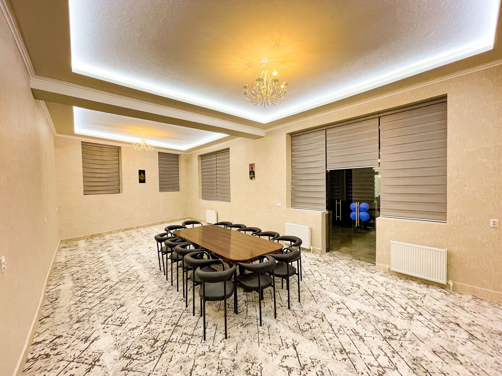A conference room with a large table and chairs, a chandelier, and large windows with blinds.