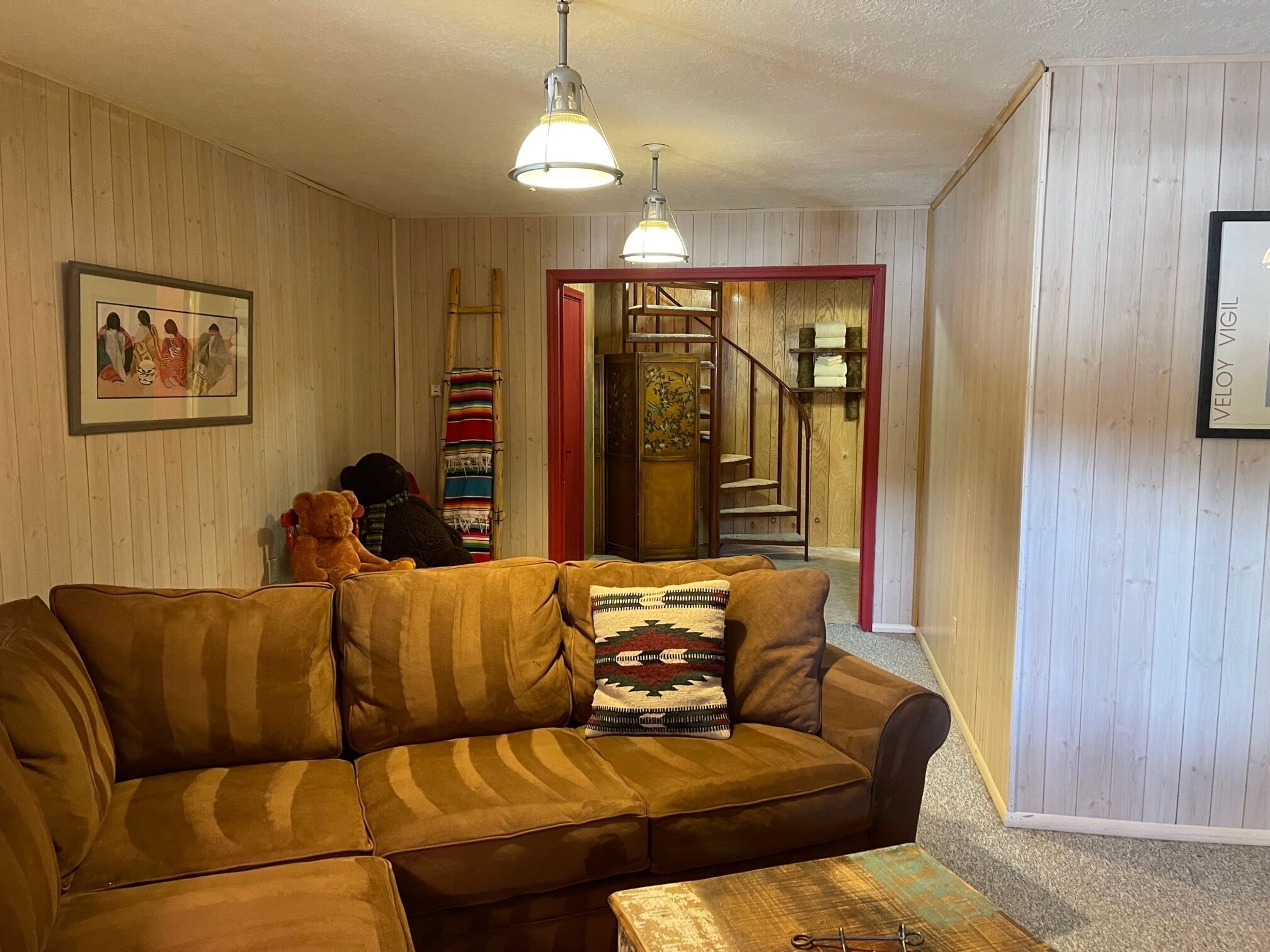A cozy living room with a brown sofa, a wooden coffee table, and a staircase leading to an upper level.