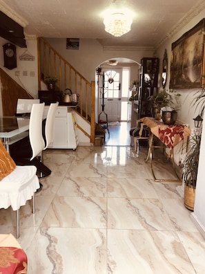 A spacious living area with a marble floor, a dining table with chairs, a staircase, and a kitchen area.