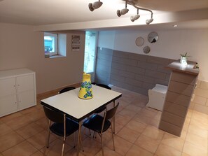 A dining area with a white table and black chairs, a yellow vase with blue flowers, and a kitchen counter with a plant.