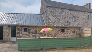 A stone building with a metal roof, a green gate, and a pink and yellow umbrella. - Small cottage in the countryside, near the sea (Lampaul-Ploudalmézeau)