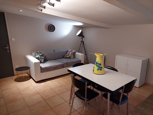 A compact living space with a sofa, a dining table with chairs, a lamp, a clock, and a cabinet.