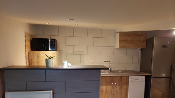 A modern kitchen with grey tiles, wooden cabinets, a built-in microwave, a stainless steel refrigerator, and a dishwasher. - Small cottage in the countryside, near the sea (Lampaul-Ploudalmézeau)