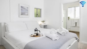 A modern hotel room with a neatly made bed, a coffee station, and a bathroom visible through an open door. - Studio 21 - walk to beach marina cafes (Nelson Bay)