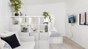 A modern, minimalist living room with a white sofa, a small side table, and a white shelving unit with books and decorative items. - Studio 21 - walk to beach marina cafes (Nelson Bay)