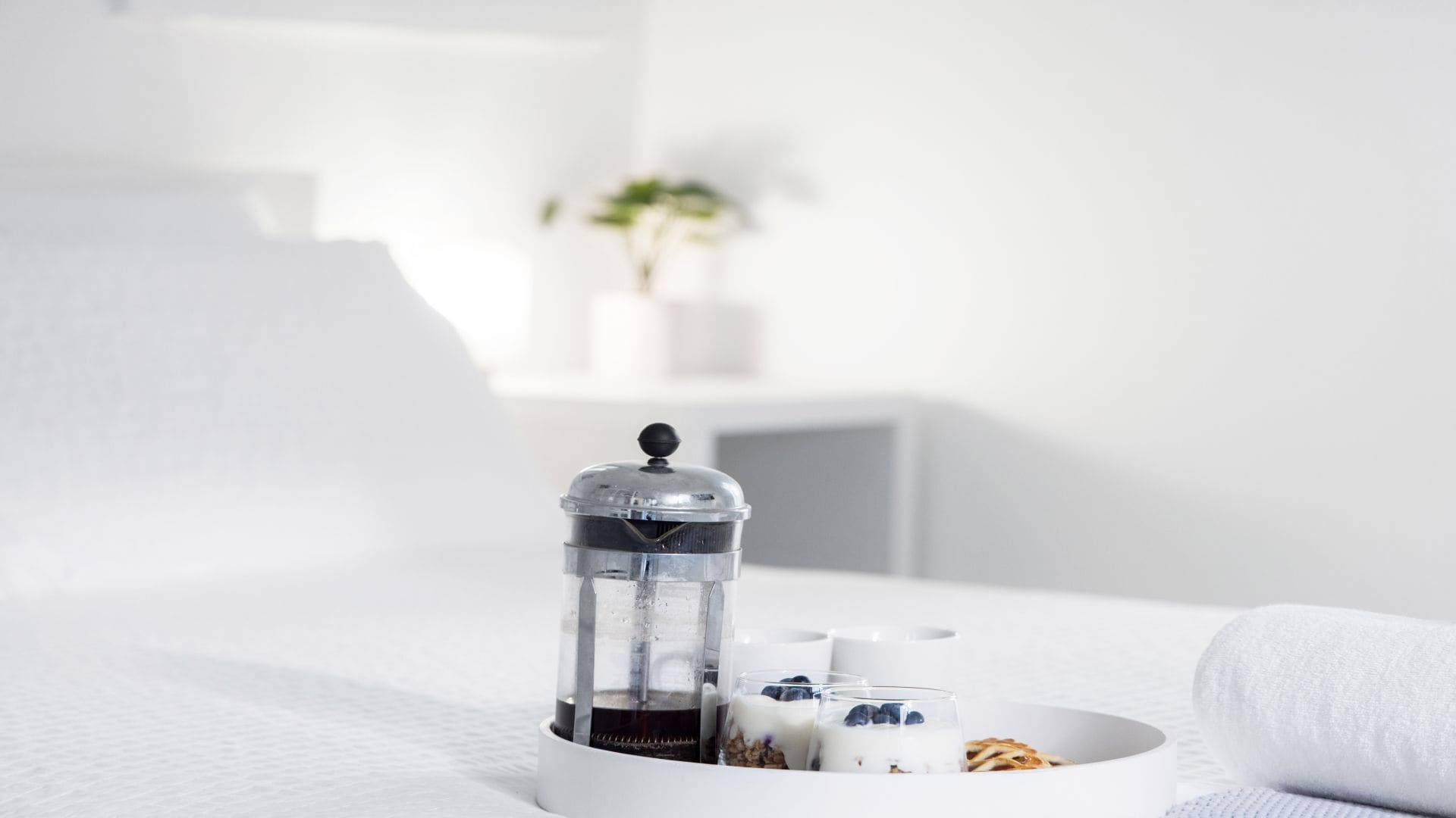 Une machine à café, un verre de lait et un bol de céréales sur une table blanche, dans une chambre d’hôtel.