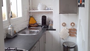 Cocina compacta con estufa a gas, lavamanos y un reloj en la pared.