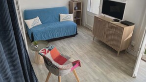 Un salón con un sofá azul, un mueble de televisión de madera, una mesita y una silla con asiento de retazos.