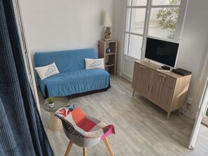 Ein Wohnzimmer mit einem blauen Sofa, einem Holz-TV-Möbel, einem kleinen Tisch und einem Sessel mit Sitzfläche aus Patchwork.