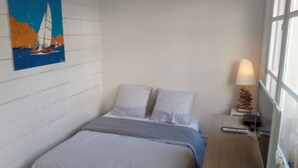 Un dormitorio con cama, almohadas, una mesita de noche con lámpara y un cuadro en la pared.