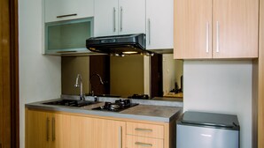 Een keuken met houten kastjes, een RVS spoelbak, een gasfornuis en een compacte koelkast.