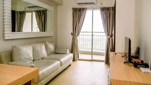 Een moderne hotelkamer met een beige bank, een houten bureau, een flatscreen televisie en een groot raam met gordijnen.