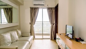 Hotelkamer met een bank, bureau met computer, airconditioning en uitzicht door een glazen deur.