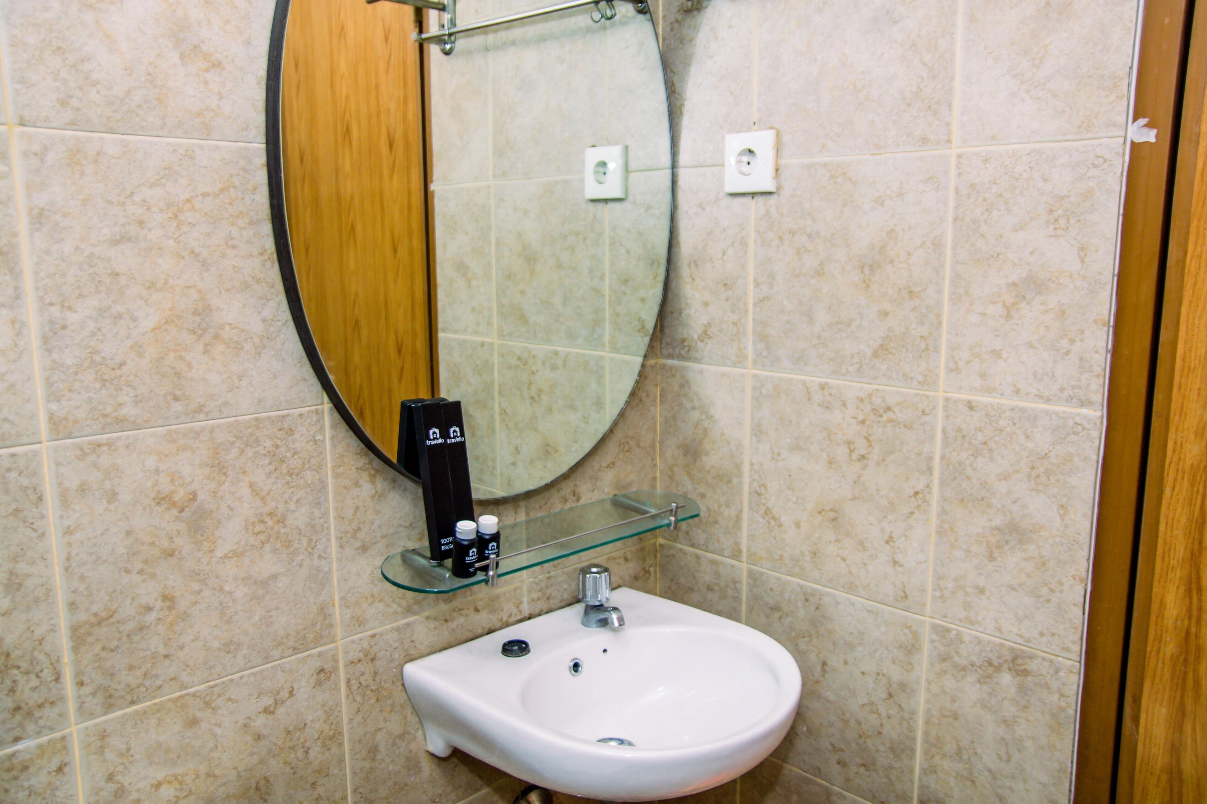 A bathroom with a round mirror, a white sink, and a glass shelf with toiletries.
