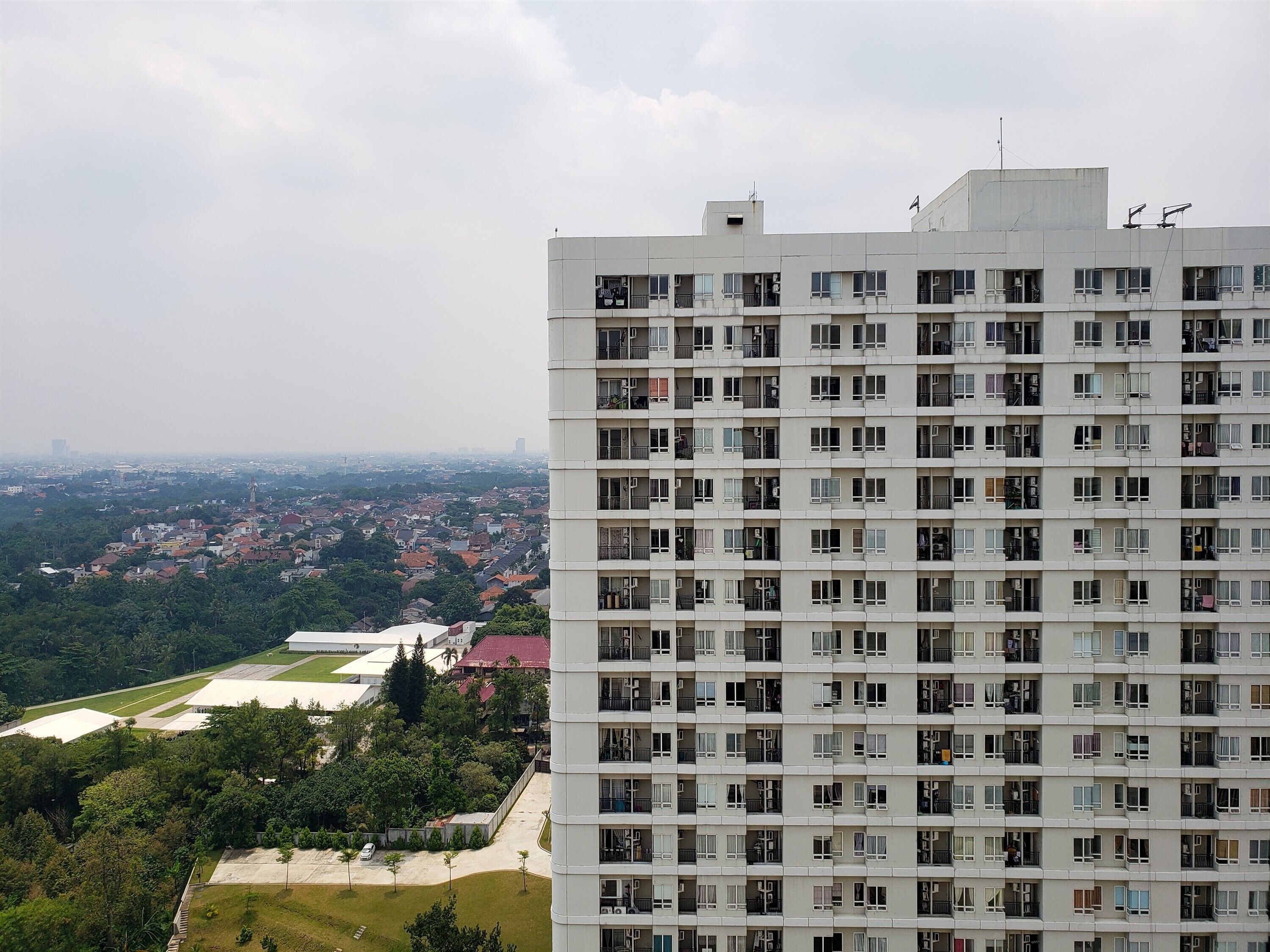 Un edificio de gran altura con varios balcones, techo plano y vistas a una zona residencial con casas y vegetación.