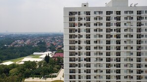 Un immeuble de grande hauteur doté de nombreux balcons, d’un toit plat et offrant une vue sur un quartier résidentiel avec des maisons et de la verdure.